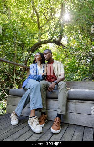Entspannendes afroamerikanisches Paar, das auf Holzbank auf Deck im Wald sitzt, mit Smartwatch sichtbar Stockfoto