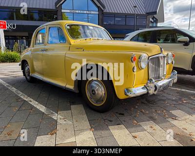 Gelber Rover P4 Oldtimer, ein klassisches Auto, parkt auf einem gepflasterten Untergrund in Taupo, Neuseeland, mit einem modernen Gebäude im Hintergrund. Stockfoto