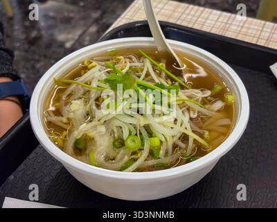 Vietnamesische Pho-Nudelsuppe mit Rindfleisch, Reisnudeln, Sojasprossen, geschnittenen Zwiebeln und frischem Koriander, serviert in einer weißen Einwegschale mit einem Löffel Stockfoto