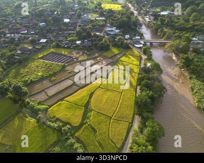 Ruhiger Blick aus der Luft von der Drohne des ländlichen Dorfes in Asien. Diese friedliche Landschaft zeigt eine wunderschöne Gemeinschaft mit Fluss, Brücke und grünem Reiseroute Stockfoto