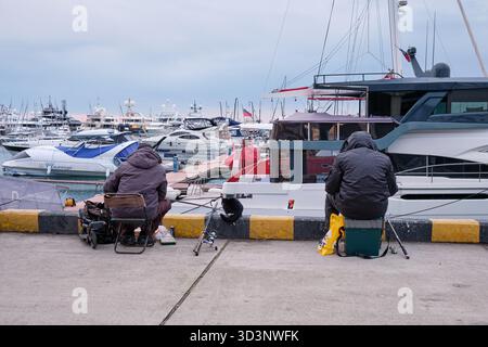 Sotschi, Russland - 15. Februar 2025: Angler sitzen auf dem Pier und warten auf den Fang. Fischer der großen Marina von Sotschi. Region Krasnodar, Russland Stockfoto