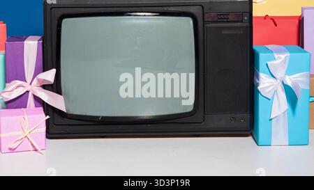 Ein altes Fernsehgerät befindet sich inmitten einer Sammlung von bunt gewickelten Geschenken und schafft eine festliche und nostalgische Szene. Stockfoto