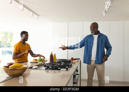 Kochen afroamerikanischer Vater und Sohn, die Burger in der Küche zubereiten, mit Salat und Messer Stockfoto
