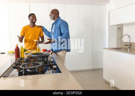 Kochen afroamerikanischer Vater und Sohn auf Kücheninsel, mit Spachtel und Smartphone, Kopierraum Stockfoto