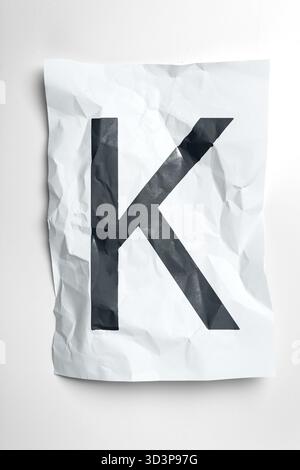 Zerknittertes Papier mit dem großen schwarzen Buchstaben K auf weißem Hintergrund Stockfoto