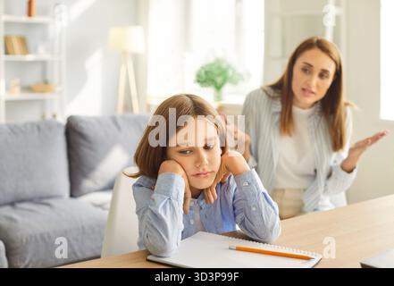 Verärgerte Mutter, die versucht, mit einem frustrierten Sohn zu sprechen, der am Schreibtisch sitzt und Augenkontakt vermeidet. Stockfoto