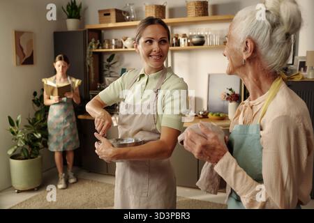 Eine weiße Frau mittleren Alters lächelt, während sie Zutaten mit der Seniorin mischt Stockfoto