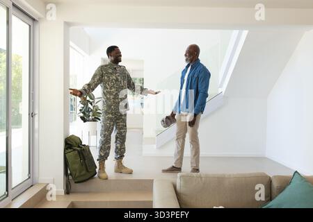 Begrüßung von afroamerikanischem Vater und Sohn, umarmt in einem modernen Hauseingang, mit Militärrucksack Stockfoto