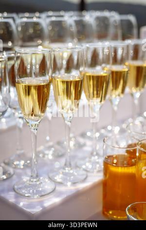 Reihen prickelnder Sektflöten auf weißem Tisch mit goldener Flüssigkeit und weichem Bokeh Stockfoto