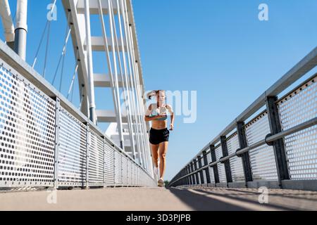 Athletische Frau, die draußen auf der Stadtbrücke läuft Stockfoto