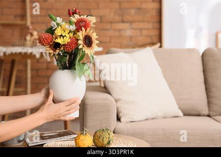 Weibliche Hände und Vase mit Herbstblumen im Wohnzimmer Stockfoto