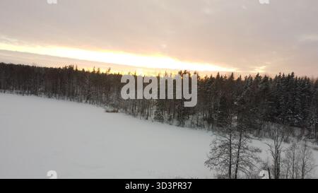 Aus der Vogelperspektive auf verschneiten Wald und gefrorenen See, die im Winterlicht bei Sonnenuntergang leuchten Stockfoto