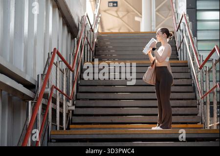 Frau in Workout-Kleidung, die auf der Treppe trinkt Stockfoto