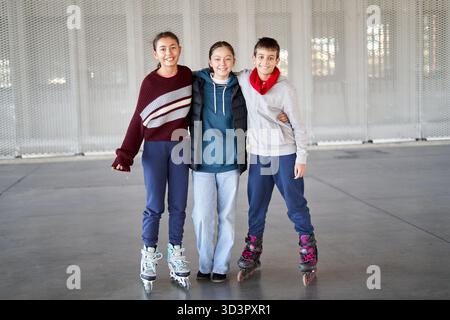 Drei Freunde, zwei Mädchen und ein Junge, gleiten auf Rollschuhen auf einer lokalen Eisbahn. Sie teilen ein Lächeln, während sie zusammen posieren und ihren Tag draußen genießen Stockfoto