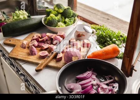 Eine Auswahl an frischem Gemüse, einschließlich Karotten, Brokkoli, Süßkartoffeln und in Scheiben geschnittenen Zwiebeln, ist auf einer Küchenzeile angeordnet, bereit zum kochen Stockfoto