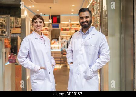 Zwei Apotheker in weißen Labormänteln stehen selbstbewusst vor einer gut bestückten Apotheke und zeigen Professionalität und Bereitschaft, mit Medicati zu helfen Stockfoto