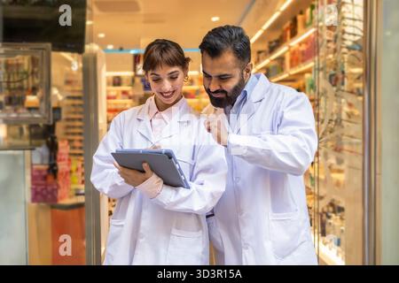 Zwei Apotheker in einer modernen Apotheke überprüfen die Medikamenteninformationen von Patienten auf einem digitalen Tablet. Sie arbeiten eng zusammen, um Genauigkeit, Sicherheit und Sicherheit zu gewährleisten Stockfoto