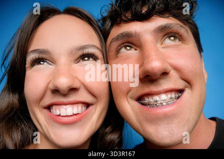 Ein Nahbild eines lächelnden jungen Paares mit blauem Hintergrund, das Freude und Freundschaft betont. Der Mann trägt eine Zahnspange und verleiht ihm einen Jugendlichen Charme Stockfoto