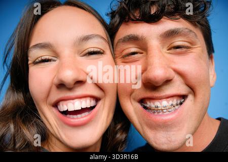 Zwei junge Freunde teilen sich einen freudigen Moment und lachen vor einem leuchtend blauen Hintergrund warm und zeigen Glück, Freundschaft und Jugendlichen Geist Stockfoto