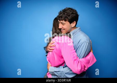 Ein junges Paar teilt eine warme Umarmung vor einem ruhigen blauen Hintergrund, der Zuneigung und Nähe vermittelt. Das Bild fängt einen intimen Moment ein, hoch Stockfoto
