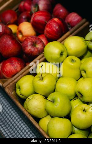 Eine lebhafte Auswahl an roten und grünen Bio-Äpfeln ist in einem Supermarkt ordentlich in Holzkisten angeordnet. Die einladende Anzeige betont Frische und Stockfoto