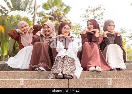 Eine Gruppe junger muslimischer Frauen in Hijabs sitzt zusammen im Freien und genießt einen sonnigen Tag. Sie lächeln und zeigen das Wesen der Freundschaft Stockfoto