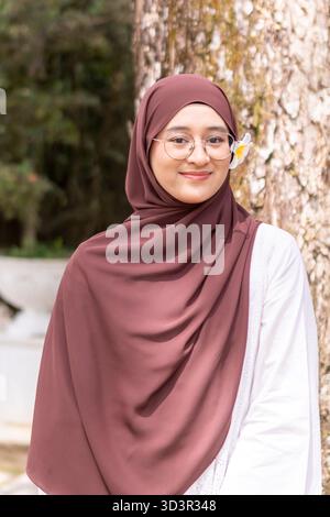 Eine junge muslimische Frau aus der Generation Z steht anmutig im Freien, trägt einen stilvollen Hijab und eine Brille. Sie strahlt Selbstvertrauen und Positivität aus, umarmen Stockfoto