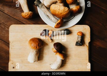 Frisch gepflückte Pilze auf einem rustikalen Holzschneidebrett und einem weißen Teller. Ideal für Herbstkochen und vegetarische Gerichte aus biologischem Anbau, Stockfoto