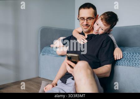 Ein Vater und sein Sohn teilen einen freudigen Moment, um gemeinsam ein Smartphone zu erkunden. Diese Szene fängt das Wesen der Familienbindung durch Technologie und ein Stockfoto