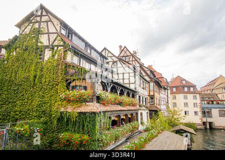 Traditionelle Fachwerkhäuser mit Blumen säumen den beschaulichen Kanal im historischen Stadtteil Straßburg, Frankreich, mit einem bezaubernden Bogen Stockfoto
