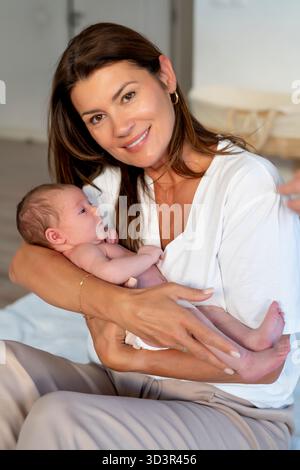 Eine liebevolle Großmutter wiegt ihre neugeborene Enkelin und lächelt in einem gemütlichen Zuhause. Dieser zärtliche Moment fängt das Wesen der Familie bondi ein Stockfoto
