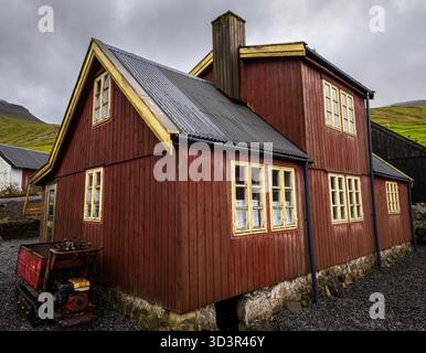 Ein bezauberndes Holzhaus mit gelb getrimmten Fenstern, eingebettet in die ruhige Landschaft der Färöer Inseln, mit rustikaler Architektur und üppigem Gier Stockfoto