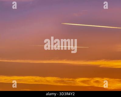 Dramatischer Sonnenuntergang Himmel mit Flugzeugkontrails über bunten Wolkenlagen Lila Orange Gelb atmosphärischer Luftfahrt Reise Hintergrund Stockfoto