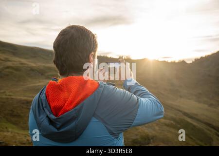 Ein Mann in einer blauen Jacke fotografiert den atemberaubenden Sonnenuntergang über den Pyrenäen. Das goldene Licht reflektiert die Landschaft und schafft eine ruhige Atmosphäre Stockfoto