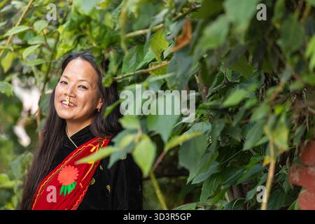 Eine nepalesische Frau steht im Freien, trägt ein traditionelles Kleid mit aufwändiger Stickerei, umgeben von üppigem Grün. Ihr helles Lächeln und ihre kulturelle Kleidung Stockfoto