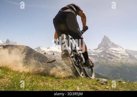 Ein Mountainbiker fährt auf einem üppigen Bergweg mit dem Matterhorn im Hintergrund und fängt den Nervenkitzel des Radfahrens in der atemberaubenden Landschaft ein Stockfoto