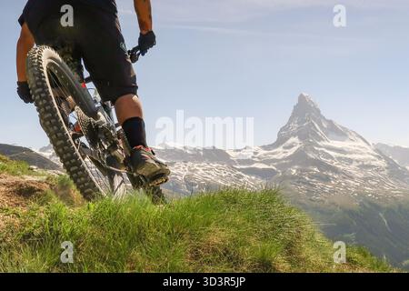 Ein Mountainbiker fährt auf einem üppigen Bergweg mit dem Matterhorn im Hintergrund und fängt den Nervenkitzel des Radfahrens in der atemberaubenden Landschaft ein Stockfoto