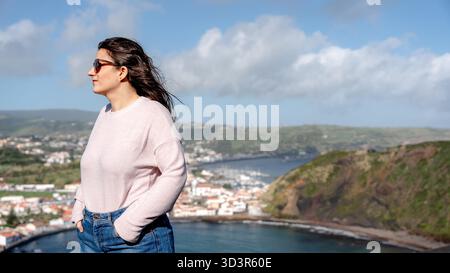 Frau in Sonnenbrille genießt die Aussicht von Miradouro da Lira auf Monte da Guia, mit Praia do Porto PIM und Monte Queimado als atemberaubender Kulisse auf Fa Stockfoto