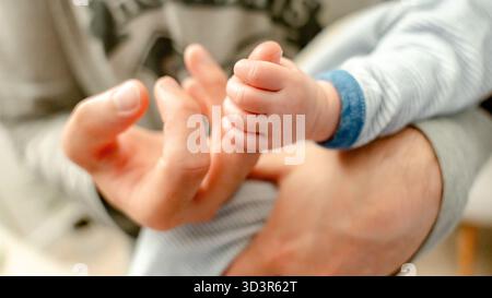 Ein Nahaufnahme-Bild, das einen zärtlichen Moment feststellt, während ein Baby sanft den Finger eines Elternteils greift. Dies symbolisiert die starke Bindung und Freude an die neue Elternschaft in a g Stockfoto
