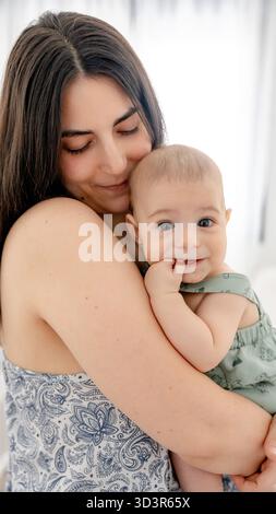 Eine liebevolle Mutter hält ihr Baby sanft fest und schafft einen berührenden Moment der Wärme und Zuneigung der Familie. Dieses Bild zeigt die frühe Entwicklung und die Entwicklung auf wunderbare Weise Stockfoto