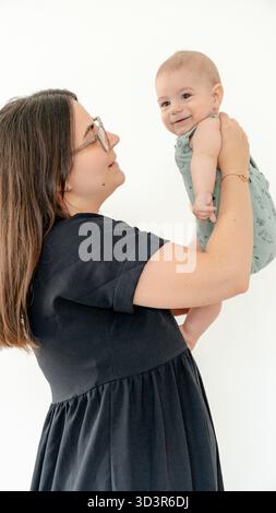 Eine fröhliche Mutter hält ihr lächelndes Baby und symbolisiert die Wärme der Familienbande und die Schönheit der frühen Entwicklung. Der Moment fängt Liebe ein, Glück Stockfoto