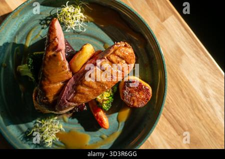 Ein perfekt gegrilltes Hähnchenfilet, serviert mit einer bunten Auswahl an gedämpftem Gemüse auf einer Keramikplatte. Das Gericht ist elegant und lebendig präsentiert Stockfoto