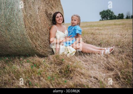 Eine ruhige Szene, in der Mutter und Tochter auf einem großen Heuballen auf einem offenen Feld in Italien sitzen und einen perfekten Moment der Familienbindung und des Countr festhalten Stockfoto