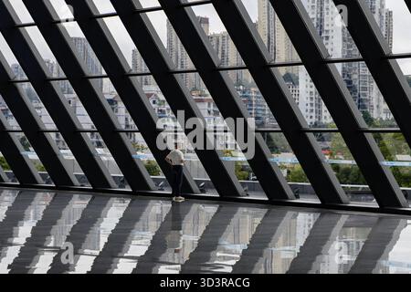 Chongqing, China - 13. Oktober 2025: Blick auf eine Einzelfigur in einem hellen, modernen Raum, eingerahmt von markanten Diagonalbalken und der fernen Stadtlandschaft Stockfoto