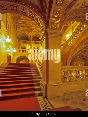 Budapest, Ungarn - 15. Oktober 2025: Blick auf die große Treppe der Ungarischen Staatsoper, wo karmesinrote Teppiche auf kunstvoll verzierte goldene Bögen treffen Stockfoto