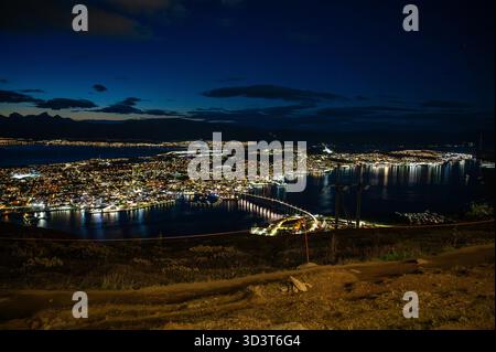 Ein atemberaubender Nachtblick auf Tromso, Norwegen, beleuchtet von Lichtern, mit einem Hafen und fernen Bergen unter einem dunkelblauen Himmel, Blick von Storsteinen Stockfoto