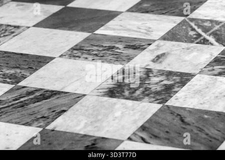 Aus nächster Nähe sehen Sie einen schwarz-weiß karierten Marmorboden mit wechselnden quadratischen Fliesen, natürlichen Adern und einem starken geometrischen Rhythmus. Archi Stockfoto