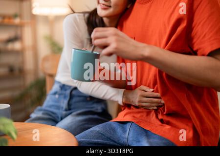 Gemütliche Momente teilen sich ein erwachsenes Paar im Haus. Warme Umarmung und Kaffeerührung sorgen für eine entspannte, liebevolle Atmosphäre. Komfort zu Hause. Stockfoto
