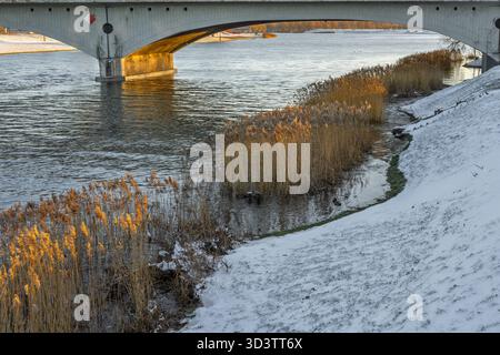 Der Boden der Brücke im Winter, schneebedeckte Ufer, die Abendsonne scheint auf die Brückenstützen, fotografiert von über dem Wasserspiegel, die Brücke i Stockfoto