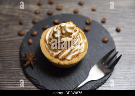 Essen, köstliche Tarte garniert mit goldgerösteten Meringue, präsentiert auf einem schwarzen Schieferteller mit verstreuten Kaffeebohnen und Sternanis Stockfoto